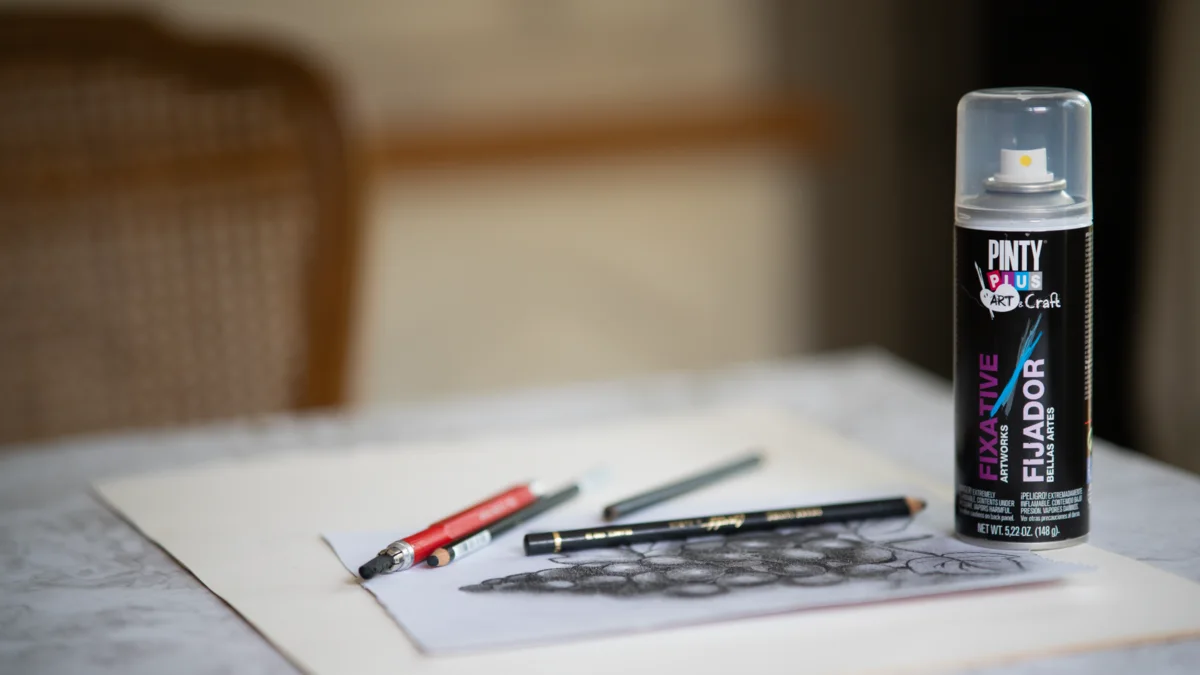 Pintyplus Fixative spray can on a table beside a pencil drawing of grapes and drawing pencils
