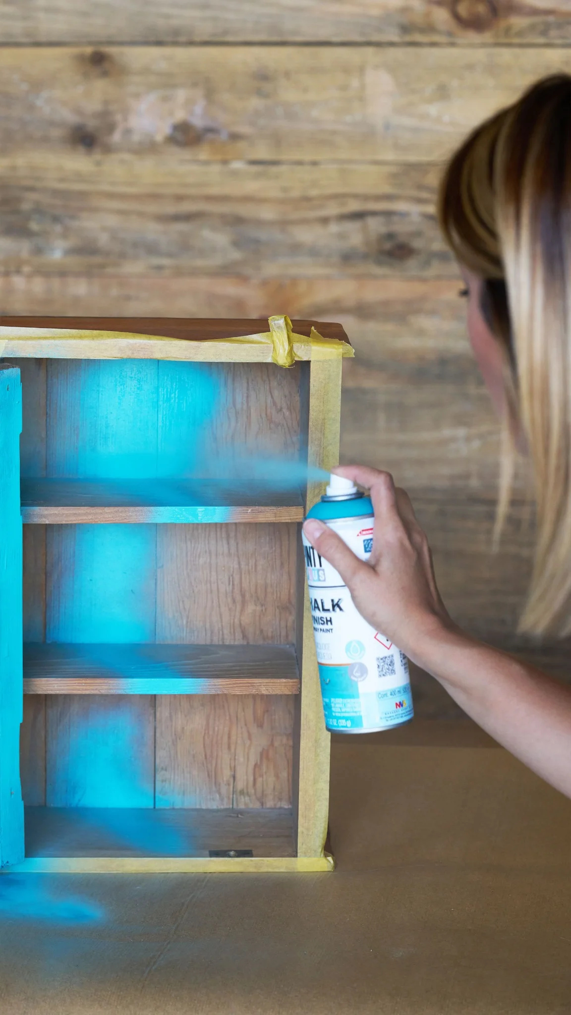 Woman spraying a small wooden shelf unit with light blue Chalk Finish paint
