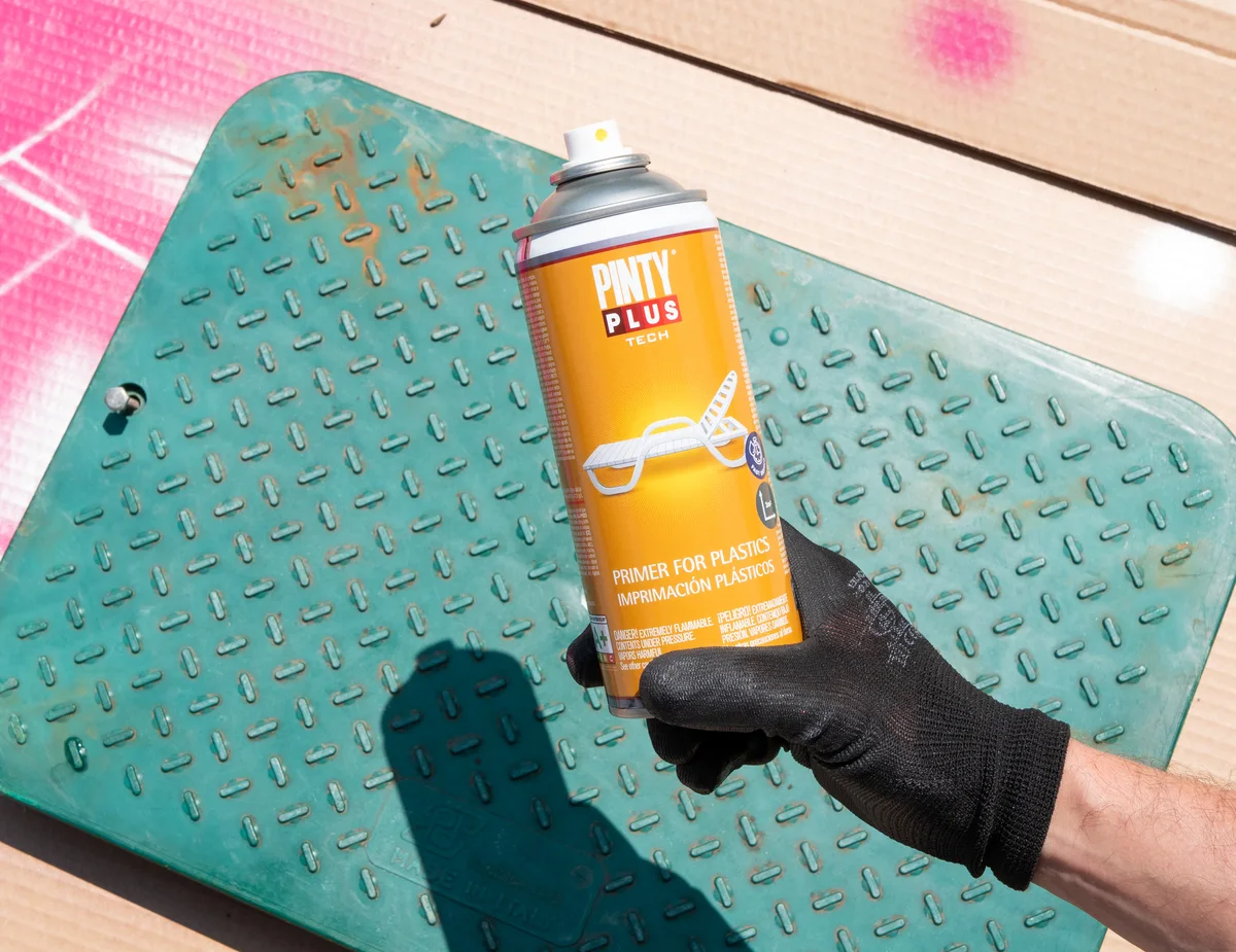 Gloved hand holding Pintyplus Primer for Plastics over a green plastic chequer-plate panel