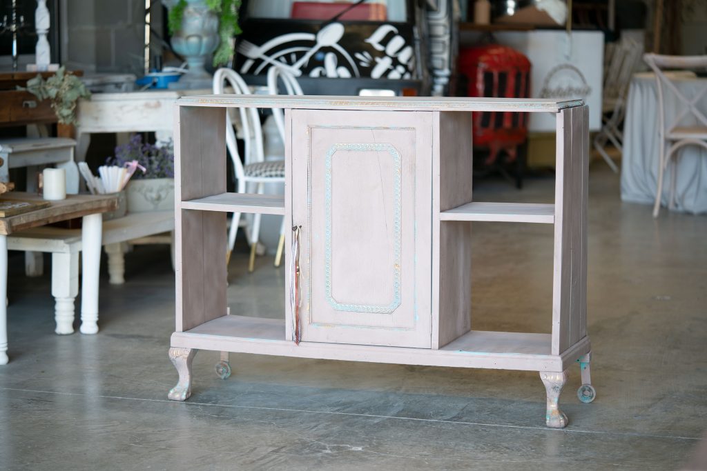 The same cabinet refreshed in a soft pink chalk finish with turquoise and gold highlights on the carved door border and legs