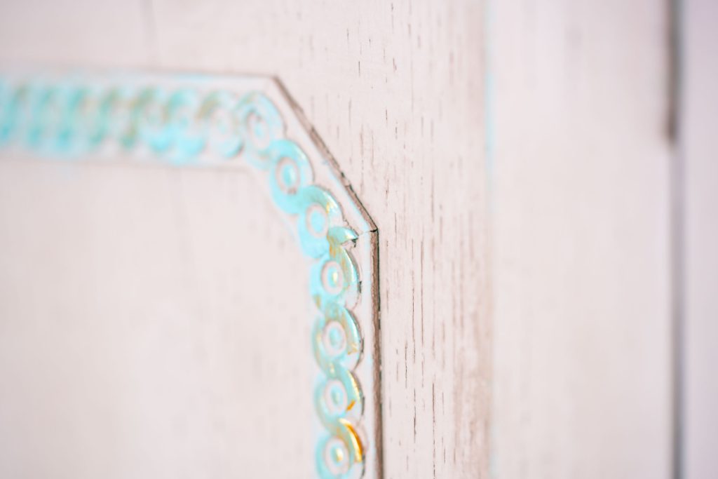 Close-up of a carved door border highlighted in turquoise with touches of gold over a pink chalk finish